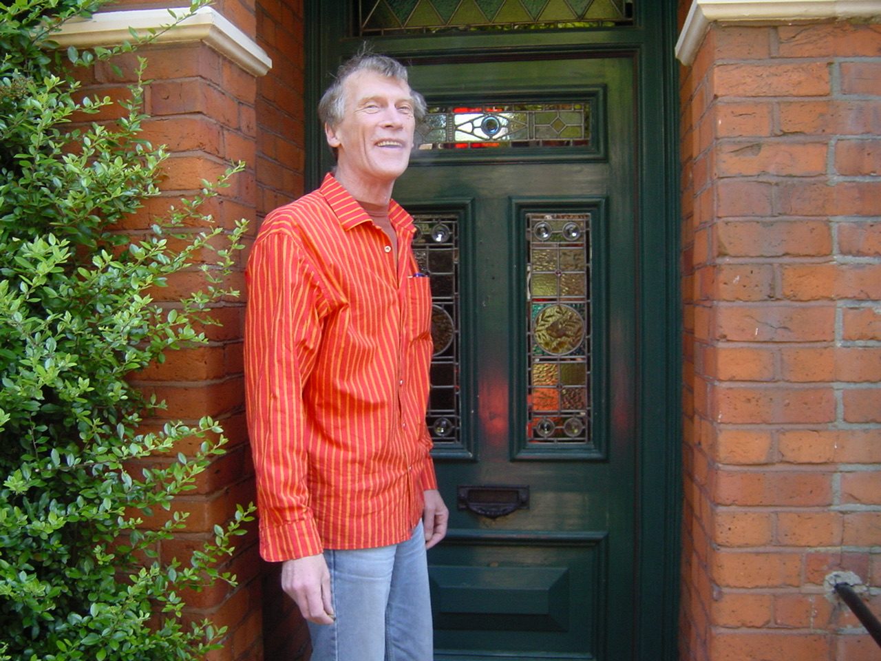 Dick Arnall smiling at the front door of the house, in a bright red and orange striped Marimekko shirt