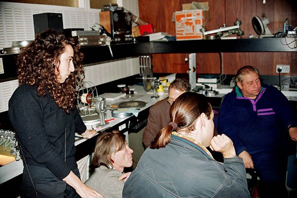 Five people gathered around film-editing equipment, with a ponytailed person seen from behind