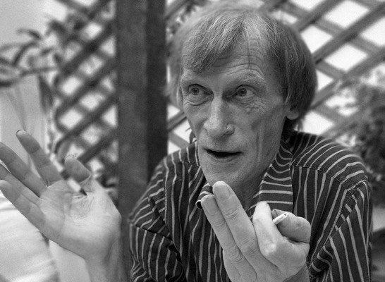 Dick Arnall in a striped shirt, mid-conversation, both hands raised, a cigarette between his fingers