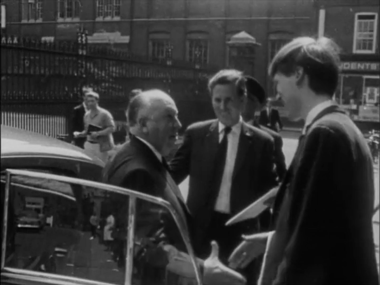Dick Arnall greeting Alfred Hitchcock beside a car in a Cambridge street, 1966